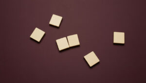 Minimalist wooden tiles on a matte burgundy background, with two tiles joined together to symbolize private equity acquisitions and business consolidation