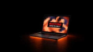 Black laptop displaying a pixelated image with a WARNING ADULTS ONLY label against a dark background.